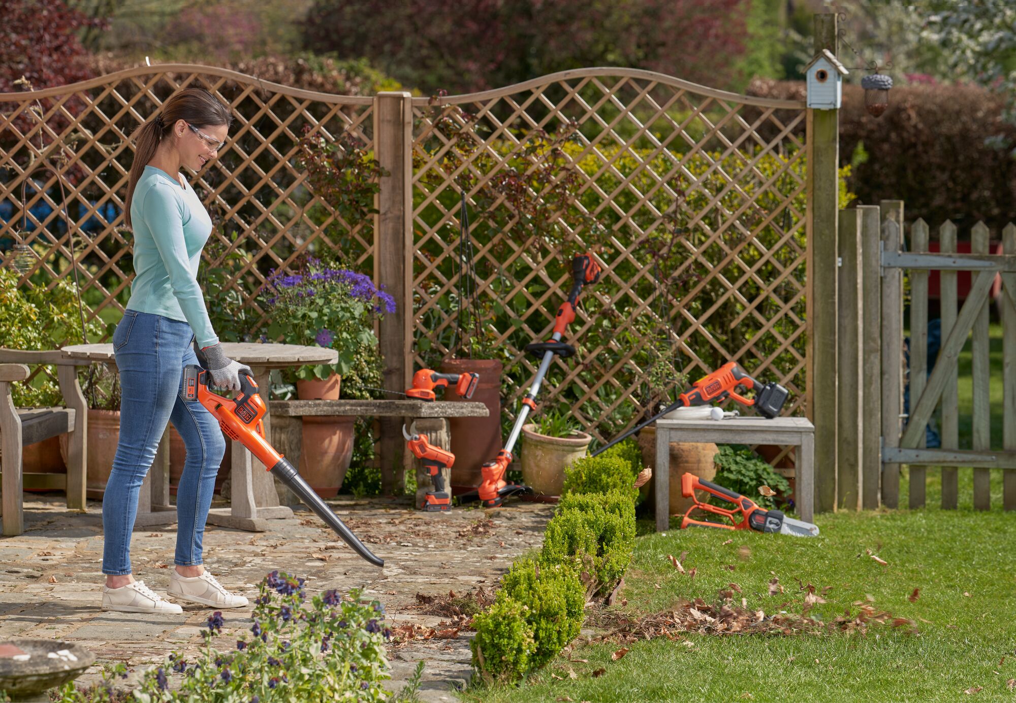 Using BLACK+DECKER Blower to clear leaves from a patio with other BLACK+DECKER POWERCONNECT garden tools in background.